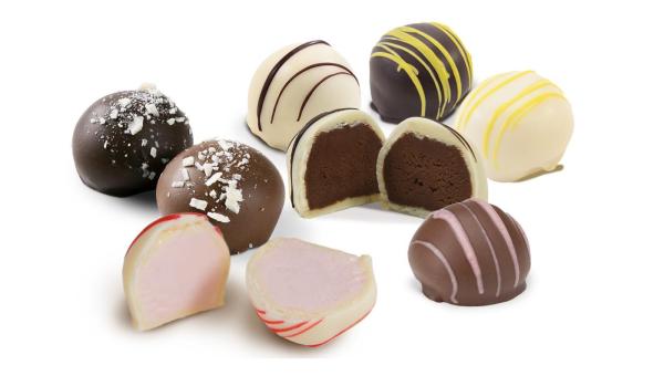 An assortment of gourmet chocolate truffles and pralines on a clean white background, including dark chocolate, milk chocolate, white chocolate, and pink chocolate varieties, with some cut open to show the filling.